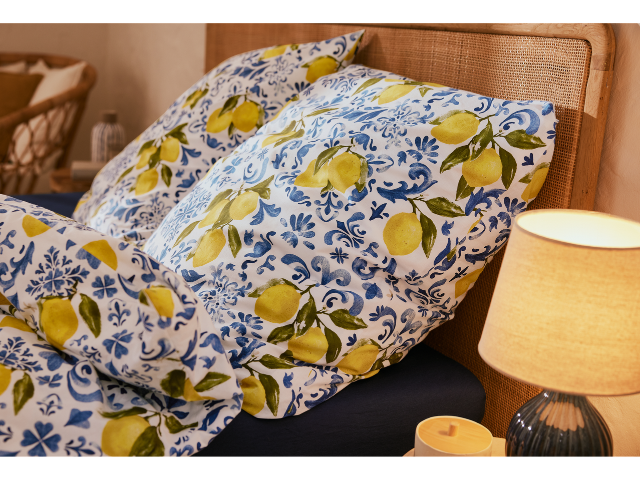 Close-up of a bed with lemon-printed bedding and a bedside lamp.