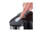Finger pressing the illuminated power button on a black and silver kettle.
