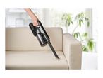 Handheld vacuum cleaner cleaning dirt from a beige sofa in a living room.