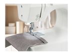 Close-up of a white sewing machine stitching a piece of grey fabric.