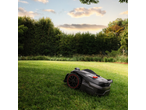 Mașină de tuns iarba robotizată autonomă pe o peluză verde cu copaci în fundal.