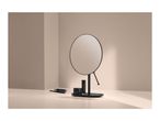 A vanity mirror with a black base, lipstick, and a small black jar on a light-colored surface.