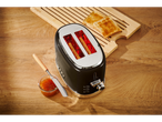 A black toaster with toast and jam on a wooden table.