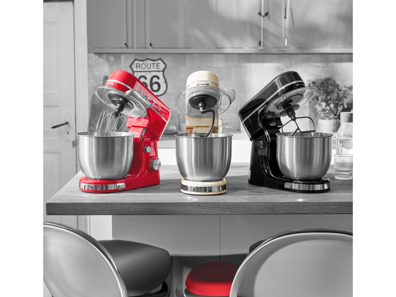 Tre impastatrici planetarie, rossa, crema e nera, su un bancone da cucina con un cartello Route 66.