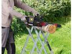 Person cutting a log with a cordless chainsaw on a sawhorse in a garden.