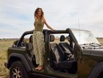 Жена стои до джип Jeep в поле.