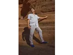 Bărbat în cămașă dungată și pantaloni bej, sprijinit de un perete de stâncă.