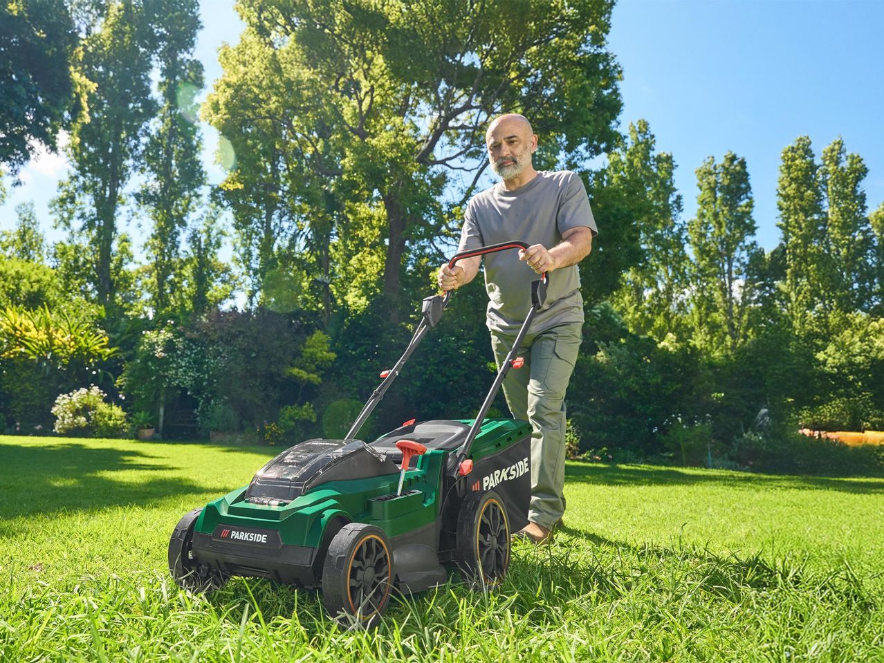 Egy férfi Parkside fűnyíróval nyírja a füvet a kertjében.
