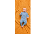 Happy baby in a blue star-patterned sleepsuit lying on an orange waffle-knit blanket.
