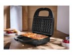 Waffle maker with two golden waffles, berries, and pancakes on a wooden table.