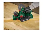 Electric planer in use on a wooden workbench, planing a piece of wood.