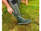 Pessoa limpando uma bota de borracha PARKSIDE com uma mangueira e bico em um jardim.