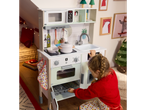 Girl playing with a white wooden play kitchen featuring an oven and microwave.