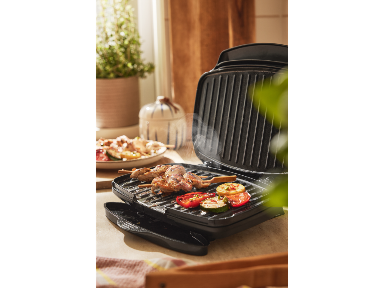 A black contact grill cooks chicken skewers and vegetables.