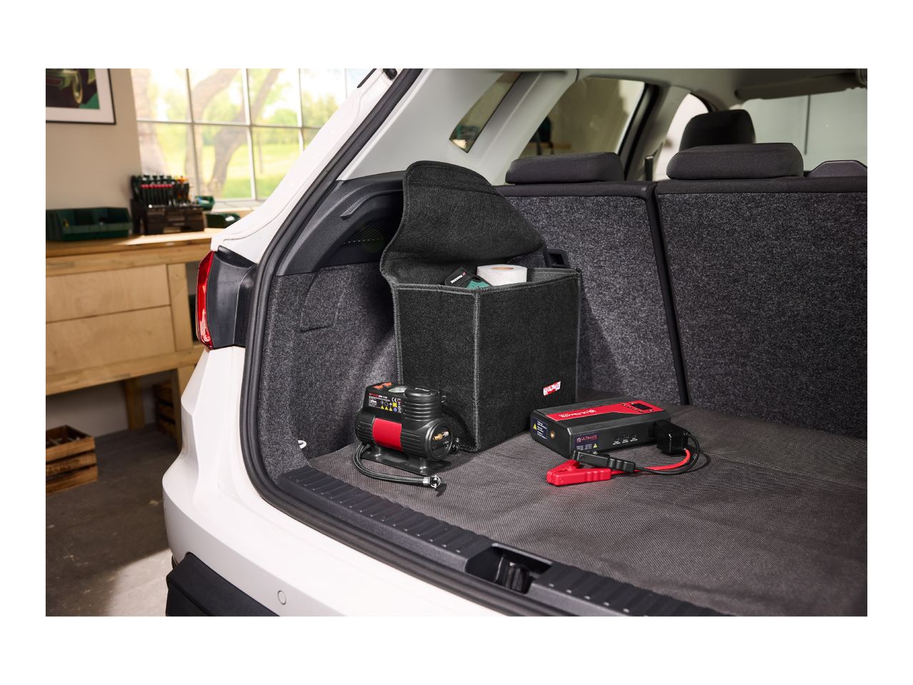 Car trunk with a tire inflator, jump starter, and storage box.