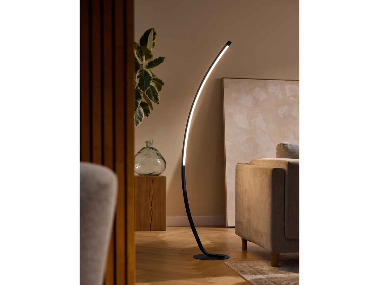 A modern arc floor lamp illuminates a living room with a beige sofa and wooden accents.