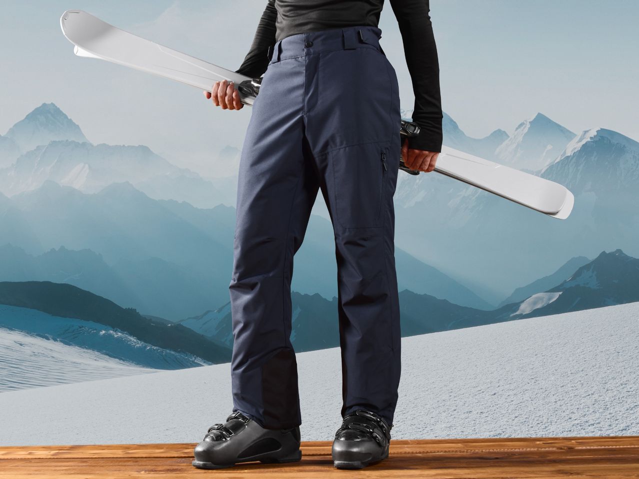 Person in dark blue ski pants and black top holding white skis, standing on a wooden deck.