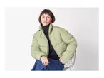 Woman in a light green puffer jacket, black turtleneck, and blue jeans, sitting on a chair.