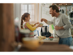 Pai e filha a cozinhar com uma máquina de cozinha, bagas e ovos no balcão.