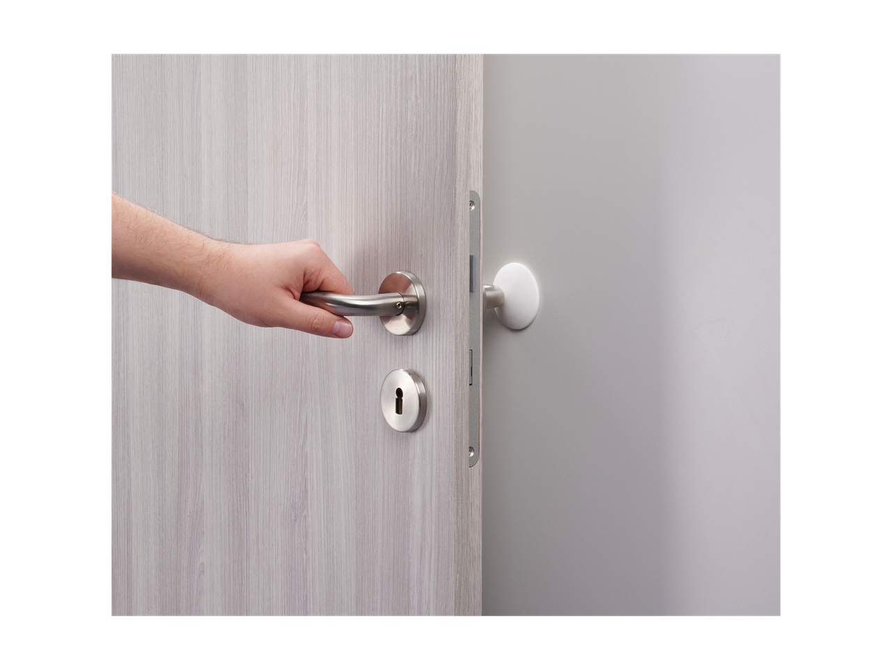 A hand reaches for a modern door handle on a light gray wood door.