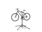 A bicycle mounted on a black repair stand with a tool tray, against a black background.