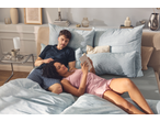 Casal a relaxar na cama com roupa de cama estampada, a ler um livro.