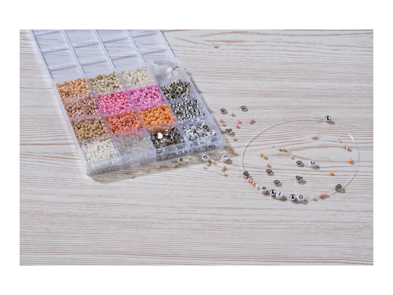 Bead organizer with various colorful beads, metal charms, and letter beads, with a partially strung necklace spelling 'RIO'.