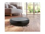 Robotic vacuum cleaner on a wooden floor with dirt, in a living room setting.