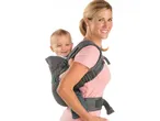 Mother with baby in a gray baby carrier, smiling at the camera.