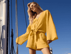 Ein Model trägt einen gelben, knotenförmigen Jumpsuit und Sonnenbrille auf einem Segelboot.