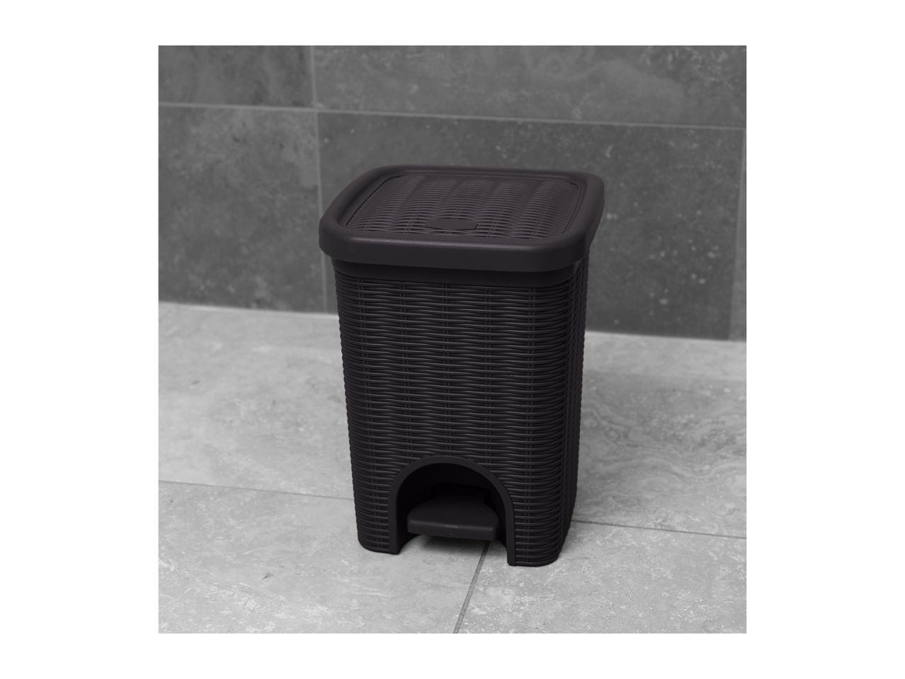Dark grey rattan-style pedal bin with a textured lid on a tiled floor.