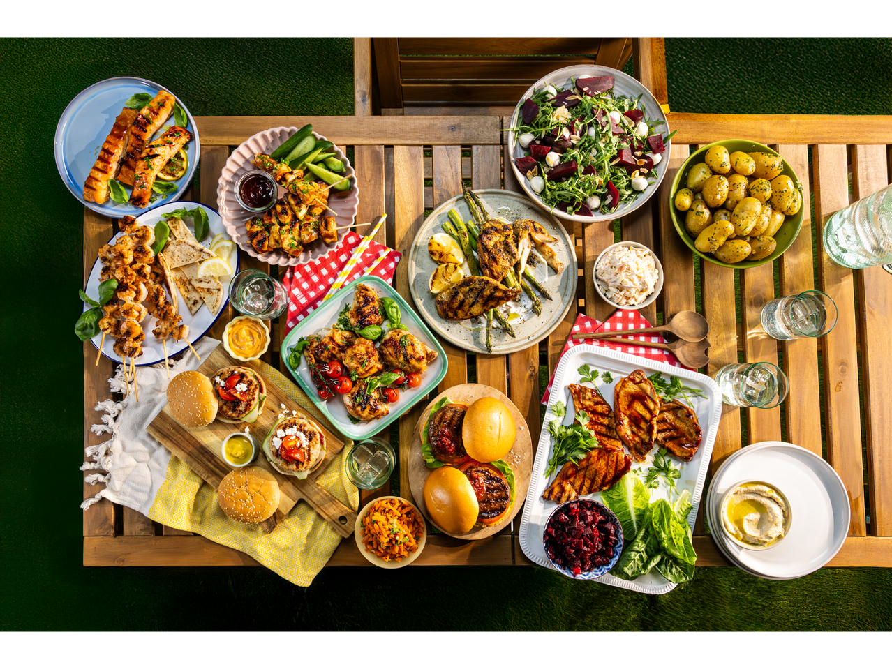 A vibrant summer picnic spread features grilled meats, salads, and sides on a wooden table.
