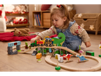 Jeune enfant jouant avec un train en bois sur le thème des dinosaures sur le sol.