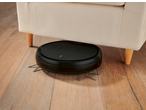 Aspirator robot negru curățând sub o canapea crem pe o podea de lemn.