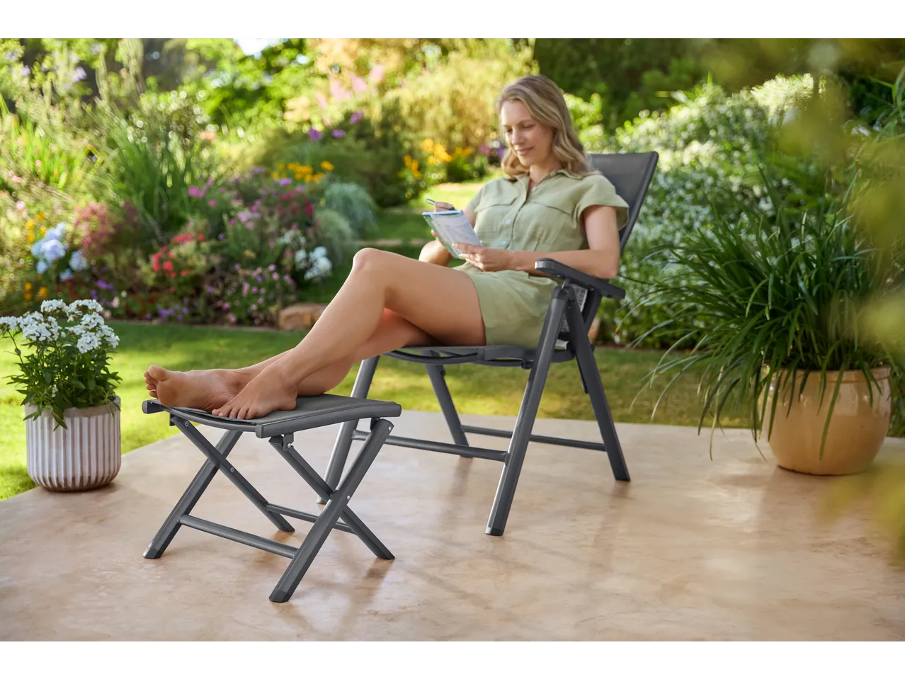 Woman relaxing in a garden chair with a footstool, writing in a notebook.