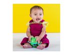 Happy baby in a magenta overall playing with a green frog toy against a yellow background.