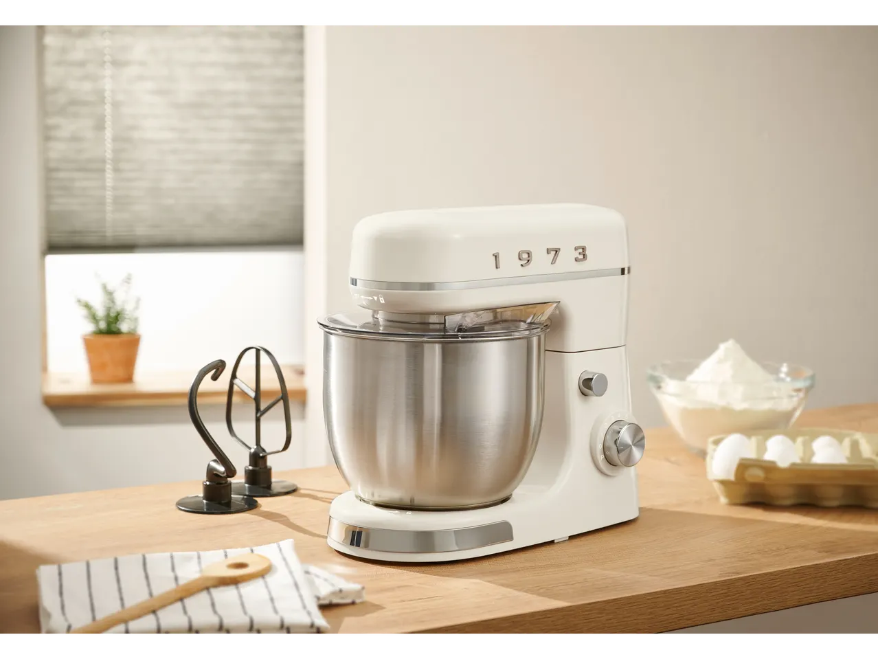 A cream-colored SILVERCREST® stand mixer with a stainless steel bowl on a wooden counter, with baking ingredients nearby.