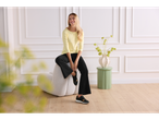 Woman in a yellow long-sleeve top and black trousers, sitting on a modern chair.