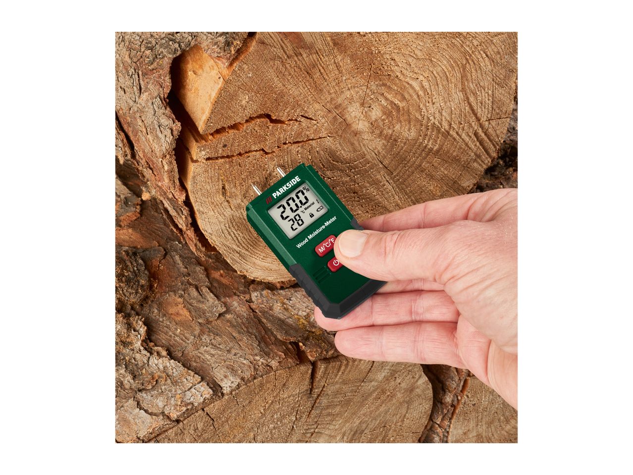 Hand holding a wood moisture meter showing 20.0% moisture and 28°C, against a background of cut logs.