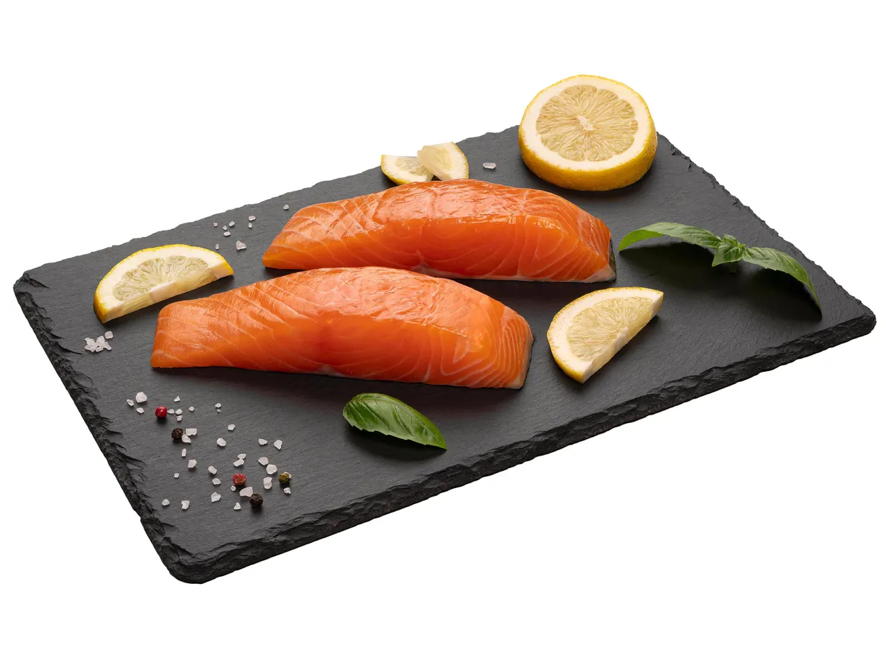 Két nyers lazacfilé citrommal, bazsalikommal és fűszerekkel egy fekete palatáblán.