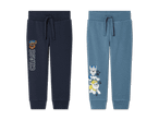 Zwei Jogginghosen mit Paw Patrol-Motiven, eine dunkelblau mit Chase, die andere hellblau mit mehreren Hunden.