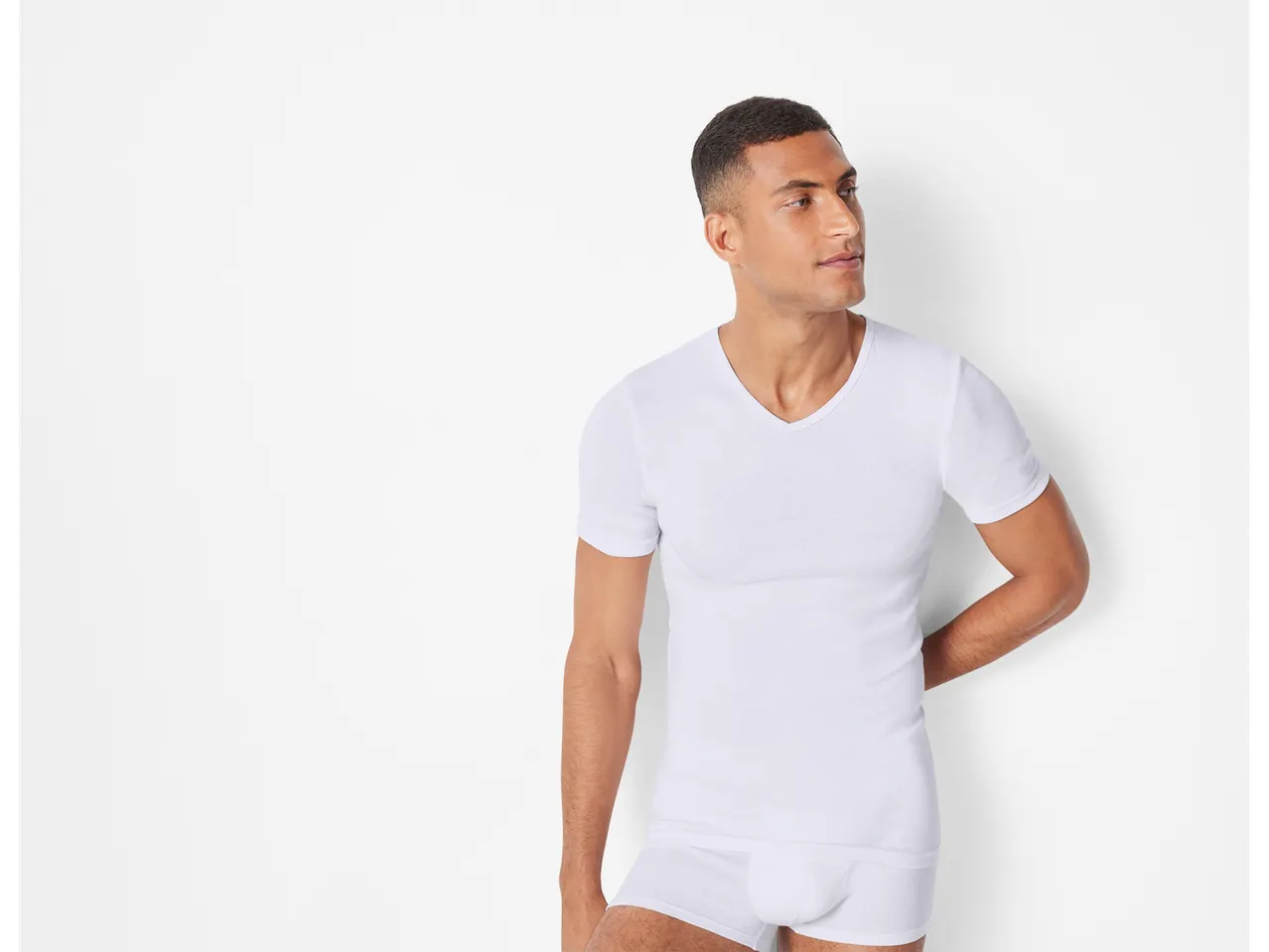 A man models a white v-neck undershirt and matching underwear.