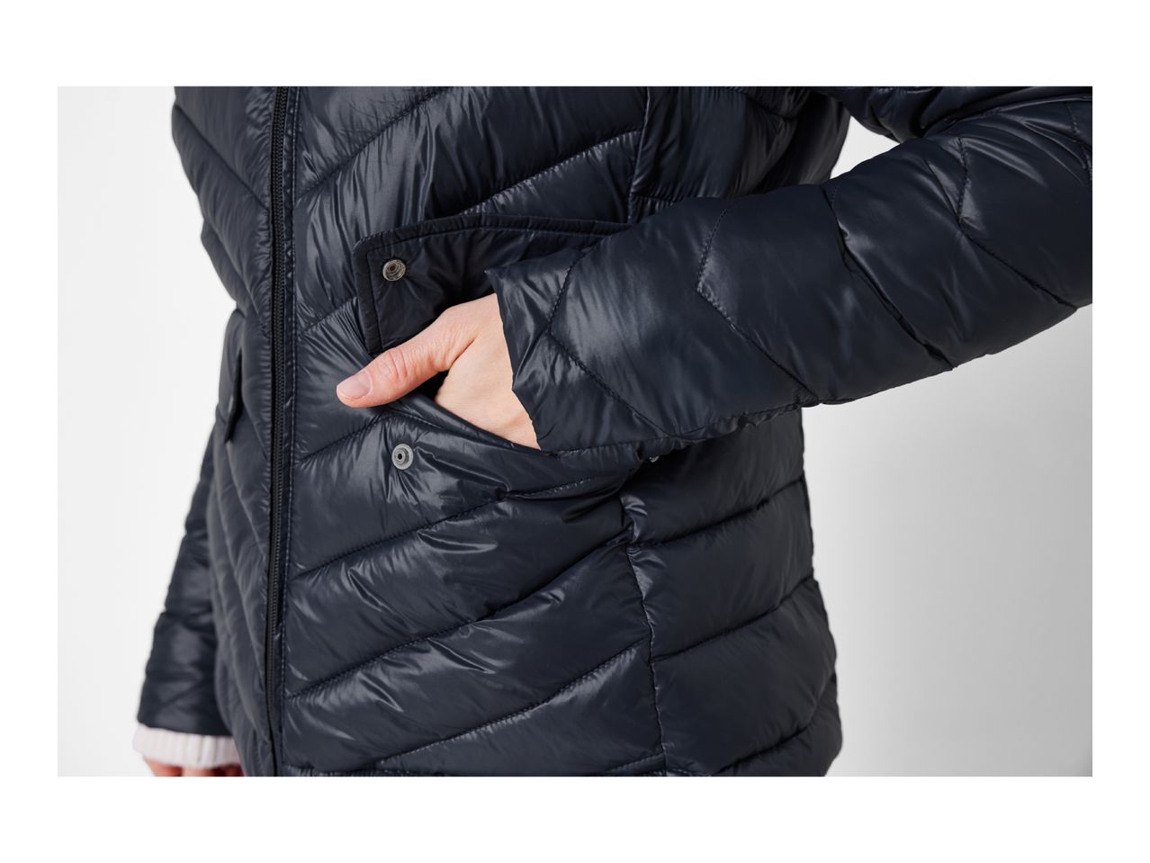 Close-up of a person wearing a dark blue quilted puffer jacket with a hand in the pocket.