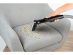 Um aspirador Cleanmaxx limpa confetes de uma poltrona cinzenta.