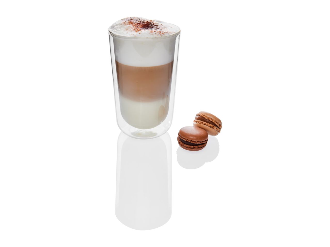 Double-walled glass holds a layered latte; two macarons sit beside it.