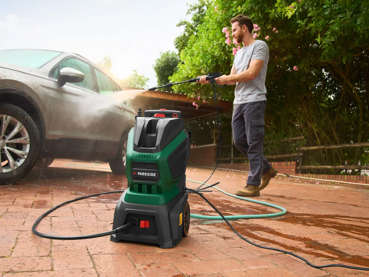 Мъж мие кола с водоструйка Parkside на павирана алея.