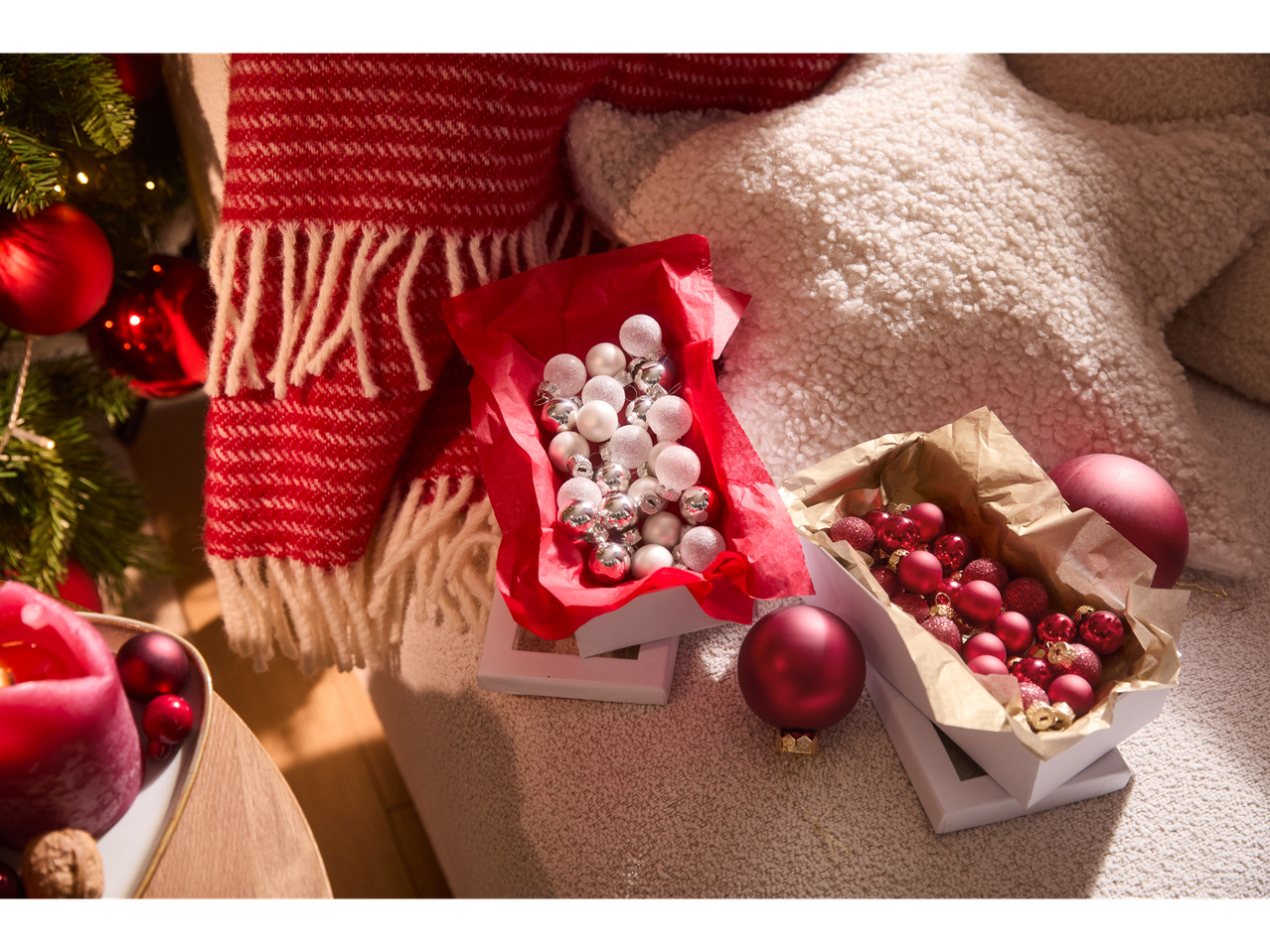 Livarno home kalėdiniai burbulai dėžutėse, raudoni ir sidabriniai, šalia eglutės ir antklodės.