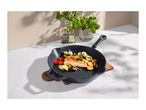 Cast iron pan with salmon, vegetables, and herbs on a white marble surface.