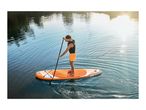Man paddleboarding on a lake with an orange paddleboard and black paddle.