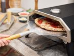 Pizza being removed from a pizza oven with a peel.